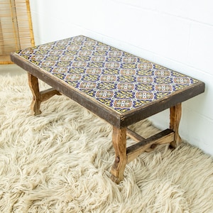 May include: A wooden coffee table with a tiled top. The tiles are a blue, yellow, and orange geometric pattern. The table has a rustic, farmhouse style.
