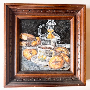May include: A framed painting of a still life with a cup of coffee, pastries, and a bottle of anise liqueur. The painting is done in a realistic style with a dark background.