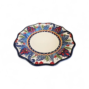 May include: A decorative ceramic plate with a scalloped edge. The plate features a cream-colored center surrounded by a blue and red floral design. The rim is dark blue, and the overall style is ornate and colorful.