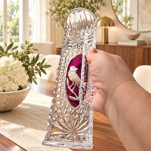 May include: A clear, tall, rectangular glass vase featuring a faceted, diamond-cut pattern across its surface. Centered on the front is an oval-shaped, deep magenta-coloured inlay depicting a silver-toned bird perched on a branch.