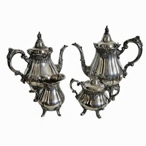 May include: A silver tea set with ornate detailing. The set includes two teapots, a creamer, and a sugar bowl. Each piece has decorative handles and feet. The set is displayed against a white background.