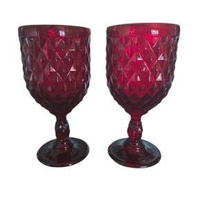 Può includere: Due calici da vino rosso rubino con motivo a diamante. I calici hanno una forma a coppa arrotondata, uno stelo e una base circolare. I calici sono in vetro e sono adatti per servire il vino.