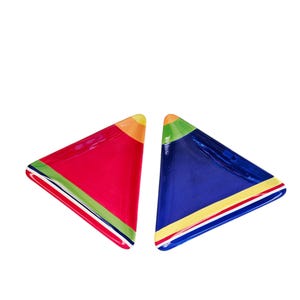 May include: Two triangular ceramic serving dishes. One is red with green and white stripes, the other is blue with yellow and white stripes. Both have orange and yellow tips. These colorful dishes are perfect for serving appetizers or snacks.
