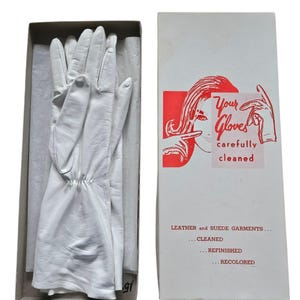 May include: White leather gloves in a box, next to a box with the text "Your Gloves carefully cleaned". The gloves are neatly arranged on tissue paper. The box has a red and white graphic of a woman.