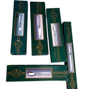 May include: A collection of boxed Shannon Fine Crystal serving utensils. The set includes a fork, cake server, slotted spoon, serving spoon, and a chef knife. The boxes are dark green with gold lettering and a diamond logo.