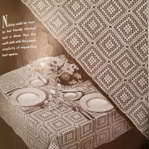 May include: A close-up of a crocheted tablecloth with a square pattern. The tablecloth is white and has a delicate, lacy design. The text "Nothing could be nicer for that friendly informal lunch or dinner than this motif cloth with the classic simplicity of repeating lacet squares." is visible in the image.