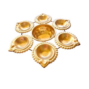 以下が含まれることがあります： 7つの個別のdiyaが付いた金色の金属製のdiyaスタンド。ディワリのお祝いに最適です。