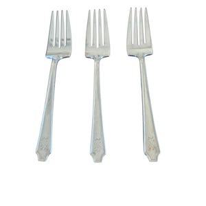 May include: Three silver forks with four tines each, arranged against a white background. The handles have a decorative floral design at the base. The forks are made of a shiny, reflective metal.