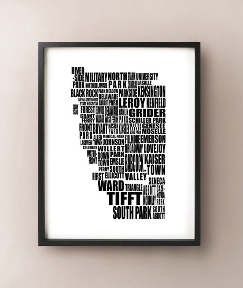 May include: Black framed art print featuring a stylized map of a city, composed entirely of place names in white font. The names are arranged to form the city's outline. The print is displayed on a neutral wall.