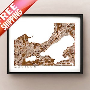 May include: Framed map print of Madison, Wisconsin, in brown and white. The city map features detailed street layouts and water bodies. The word "MADISON" is printed in a serif font at the bottom of the print. The print is in a black frame.