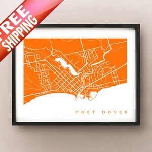 Może przedstawiać: Oprawiony wydruk artystyczny przedstawiający białą mapę Port Dover, Ontario, Kanada, na pomarańczowym tle. Nazwa miasta jest wydrukowana czcionką szeryfową na dole. Wydruk jest w czarnej ramie.