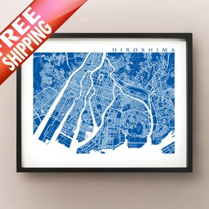 Puede incluir: Impresión enmarcada de un mapa de Hiroshima, Japón, en azul y blanco. El diseño de la ciudad está detallado, con el nombre 'Hiroshima' en la parte superior. La impresión está dentro de un marco negro.