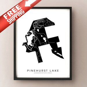May include: Black and white framed print of Pinehurst Lake Conservation Area. The artwork features a minimalist map design with the lake's outline and surrounding details. The text "PINEHURST LAKE CONSERVATION AREA" is displayed at the bottom. A red banner with the text "FREE SHIPPING" is in the upper left corner.