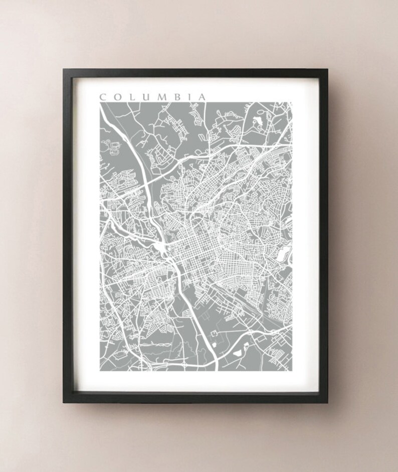 May include: Framed print of a map of Columbia, South Carolina, in white against a gray background. The city name is printed in white at the top. The map is detailed, showing streets and roads.
