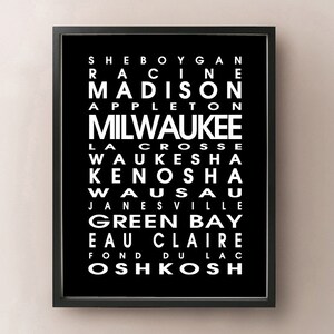 May include: Black framed print featuring a list of Wisconsin city names in white, including Milwaukee, Madison, and Green Bay. The text is arranged vertically on a black background.