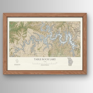 May include: A framed map of Table Rock Lake in Missouri. The map shows the lake's shoreline, islands, and surrounding terrain. The map is printed on a cream-colored paper with brown and blue accents. The frame is made of wood and has a natural finish.