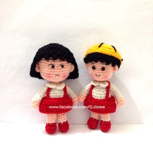 May include: Two handmade crochet dolls. One doll has black hair and the other has a yellow hat. Both dolls are wearing red dresses with white shirts underneath. The dolls are holding hands. The dolls are on a white background.