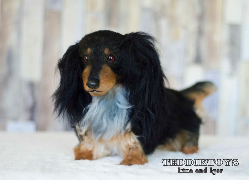 May include: A black and brown dachshund plush toy with long black fur and red eyes. The toy is lying on a white surface. The text "TEDDIKTOYS Irina and Igor" is visible in the bottom right corner of the image.