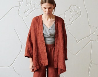 May include: A rust-colored linen pantsuit with a wide-leg, cropped pant and a long-sleeved, open-front jacket. The model is wearing the suit with a gray tank top underneath.