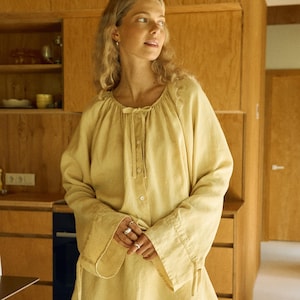 Pode incluir: Vestido de linho amarelo claro com mangas compridas e saia rodada. O vestido apresenta um decote redondo com detalhe de la&ccedil;o e fecho de bot&otilde;es. As mangas t&ecirc;m la&ccedil;os nos punhos. O vestido &eacute; at&eacute; ao joelho.