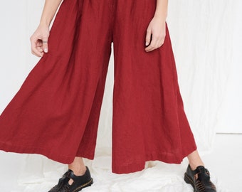 Puede incluir: Una mujer lleva una blusa de lino roja y pantalones anchos. Lleva sandalias de cuero negro.