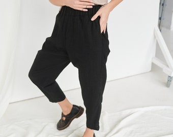 May include: A beige sleeveless top and black pants. The top has a simple, round neckline. The black pants have a relaxed fit with a gathered waist. The outfit is paired with black leather shoes with buckles.