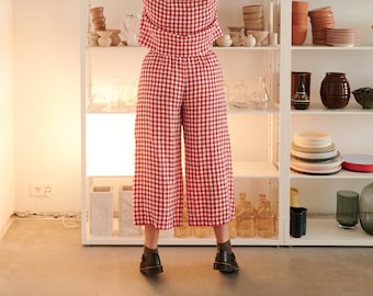 May include: A person wearing a red and white gingham outfit reaching for a large ceramic vase on a white shelf. The shelf displays various ceramic vases, bowls, and plates. The room has a minimalist design with a neutral color palette.