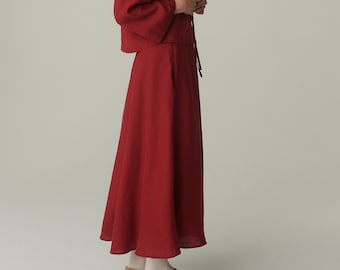 May include: A woman wearing a red linen top and skirt. The top has a tie at the neck and the skirt is a-line. She is wearing brown shoes.