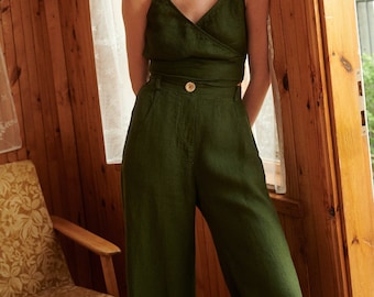 May include: A woman wearing a green linen wrap top and matching wide-leg pants. She is standing in a wooden doorway with a window behind her.
