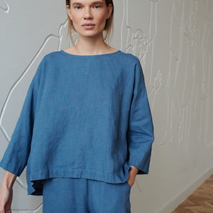 Könnte beinhalten: Ein blaues Leinenoberteil und eine passende Hose. Das Oberteil hat eine lockere Passform und einen runden Ausschnitt. Die Hose hat eine gerade Beinpartie.