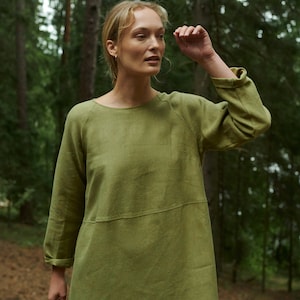 Peut inclure: Une femme portant une robe en lin vert olive &agrave; manches longues dans un d&eacute;cor forestier.