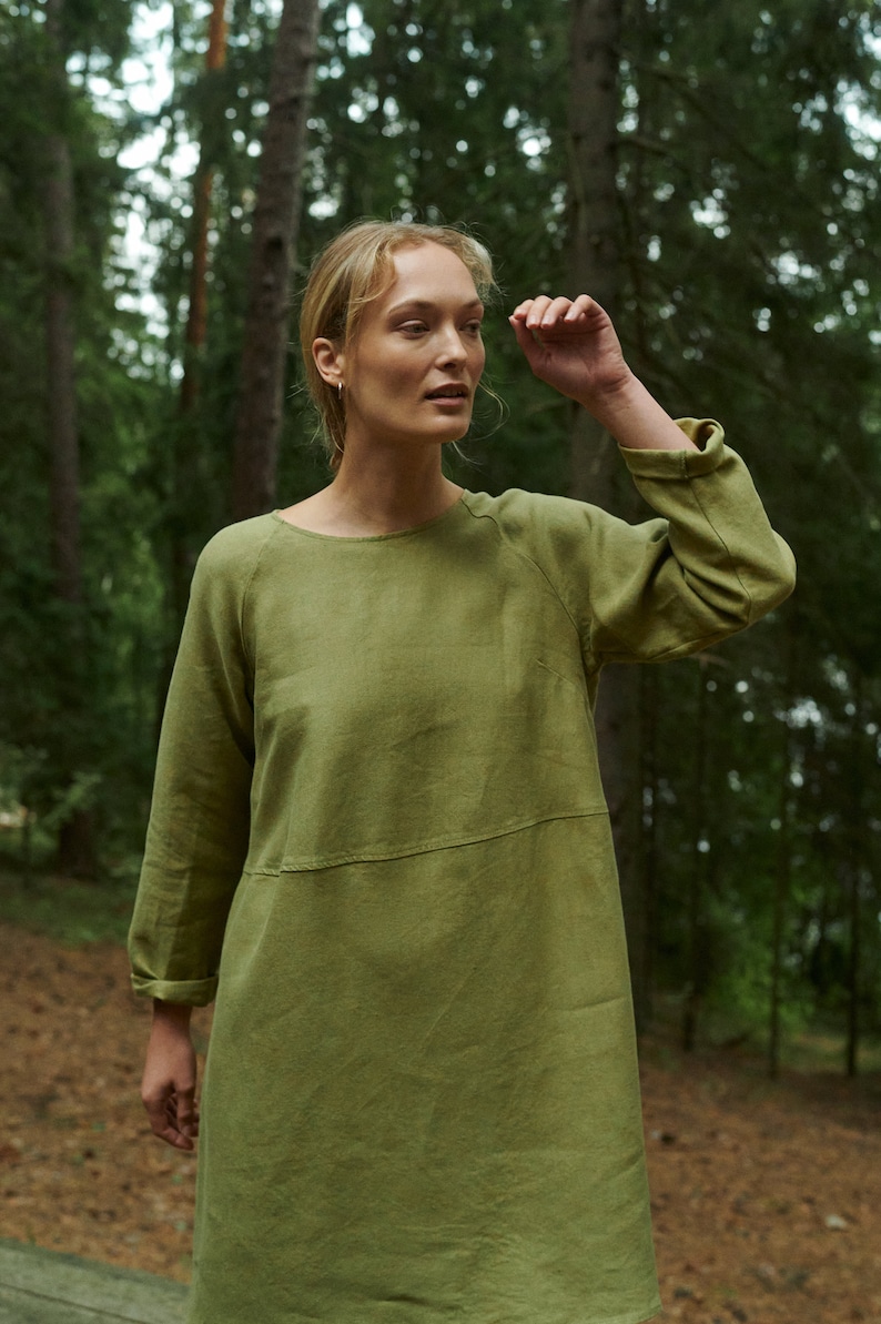 Peut inclure: Une femme portant une robe en lin vert olive &agrave; manches longues dans un d&eacute;cor forestier.