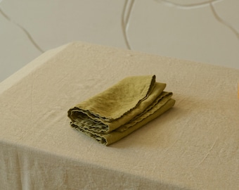 May include: A folded green linen napkin on a beige linen tablecloth.