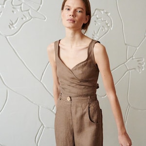 May include: A woman wearing a brown linen wrap top and matching wide-leg pants. The top has a V-neckline and a button closure at the waist. The pants have a high waist and pockets on the sides.
