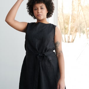 May include: A black sleeveless linen dress with a tie belt. The dress is knee-length and has a simple, classic design.