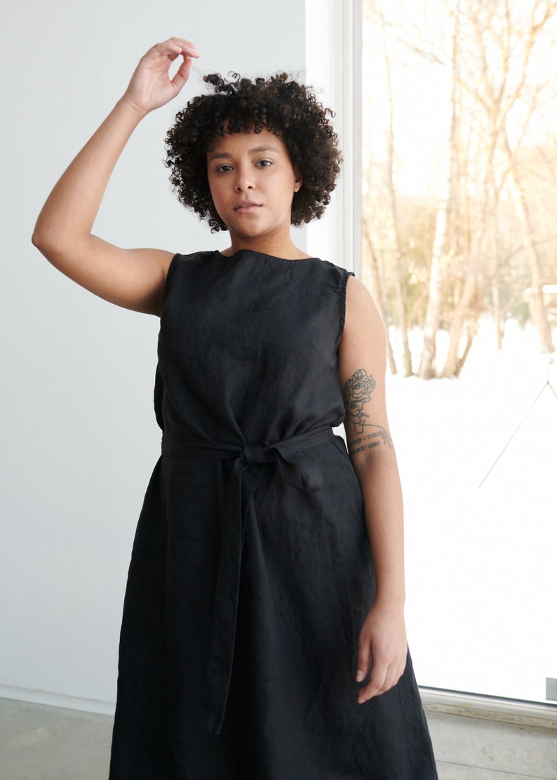 May include: A black sleeveless linen dress with a tie belt. The dress is knee-length and has a simple, classic design.