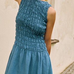 May include: A sleeveless, blue dress with a textured bodice and a flowing skirt. The bodice has a gathered, ruched design, and the skirt flares out from the waist. The dress is made of a soft, lightweight fabric, perfect for warm weather.