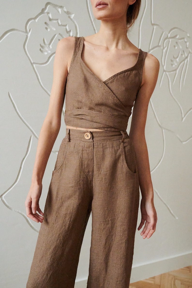 May include: A brown linen wrap top and wide-leg pants set. The top has a V-neckline and a wrap closure at the waist. The pants have a high waist and side pockets.