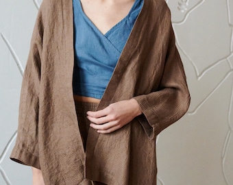 May include: A brown linen kimono with a long, loose fit and a wide, open front. The kimono has a textured weave and is worn over a blue linen top.