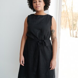 May include: A black linen dress with a tie belt. The dress has a scoop neck and sleeveless design.