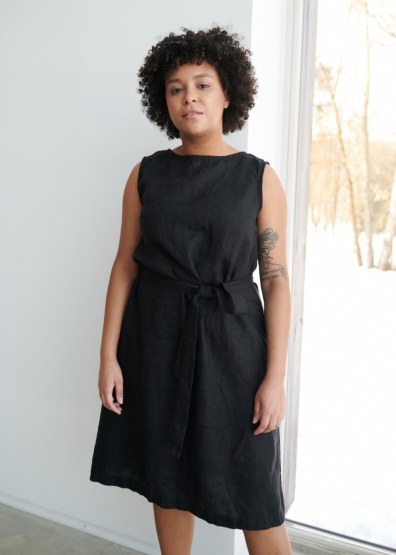 May include: A black linen dress with a tie belt. The dress has a scoop neck and sleeveless design.