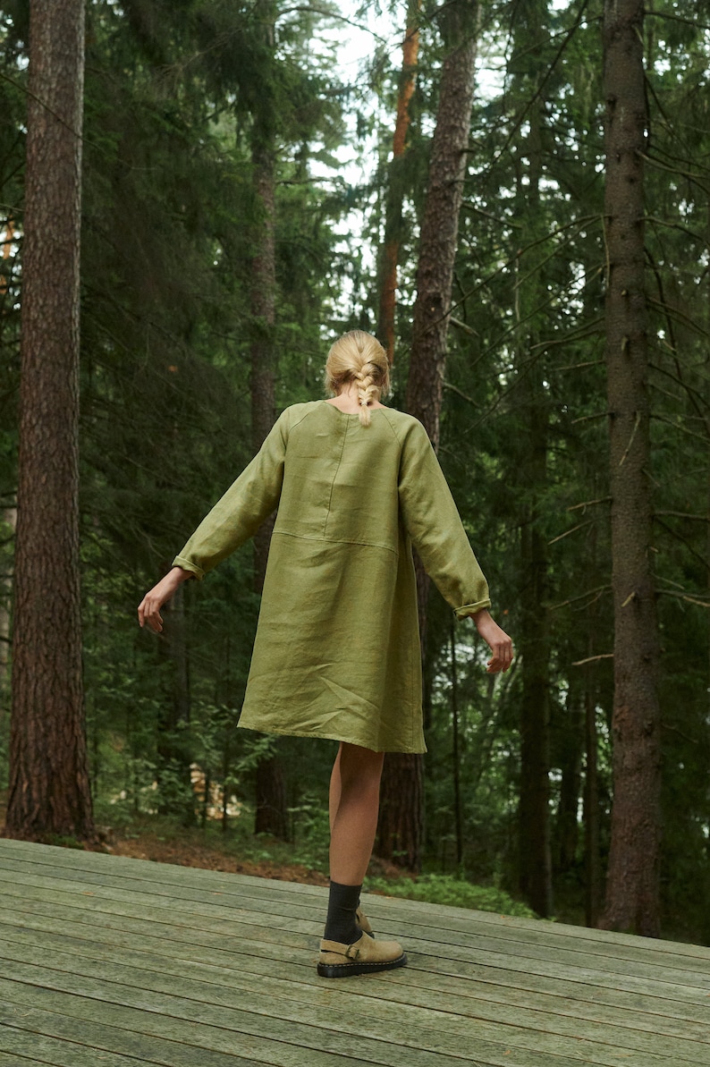 Peut inclure: Une femme portant une robe en lin vert et des chaussettes noires se tient sur une plateforme en bois dans une for&ecirc;t. Elle regarde loin de l'appareil photo.