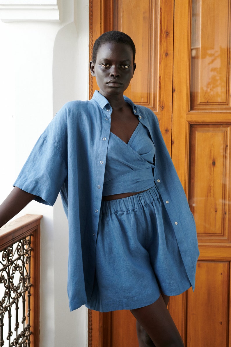 May include: A blue linen shirt and matching shorts set. The shirt has a button-down front and short sleeves. The shorts have an elastic waistband and a relaxed fit.