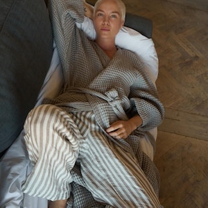 May include: A person wearing a gray waffle-weave robe with a striped pattern and a white background. The robe is tied at the waist and the person is lying on a bed.