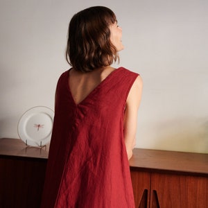 May include: A woman wearing a sleeveless, deep red linen dress with a V-neckline. The dress is loose-fitting and falls to her knees.