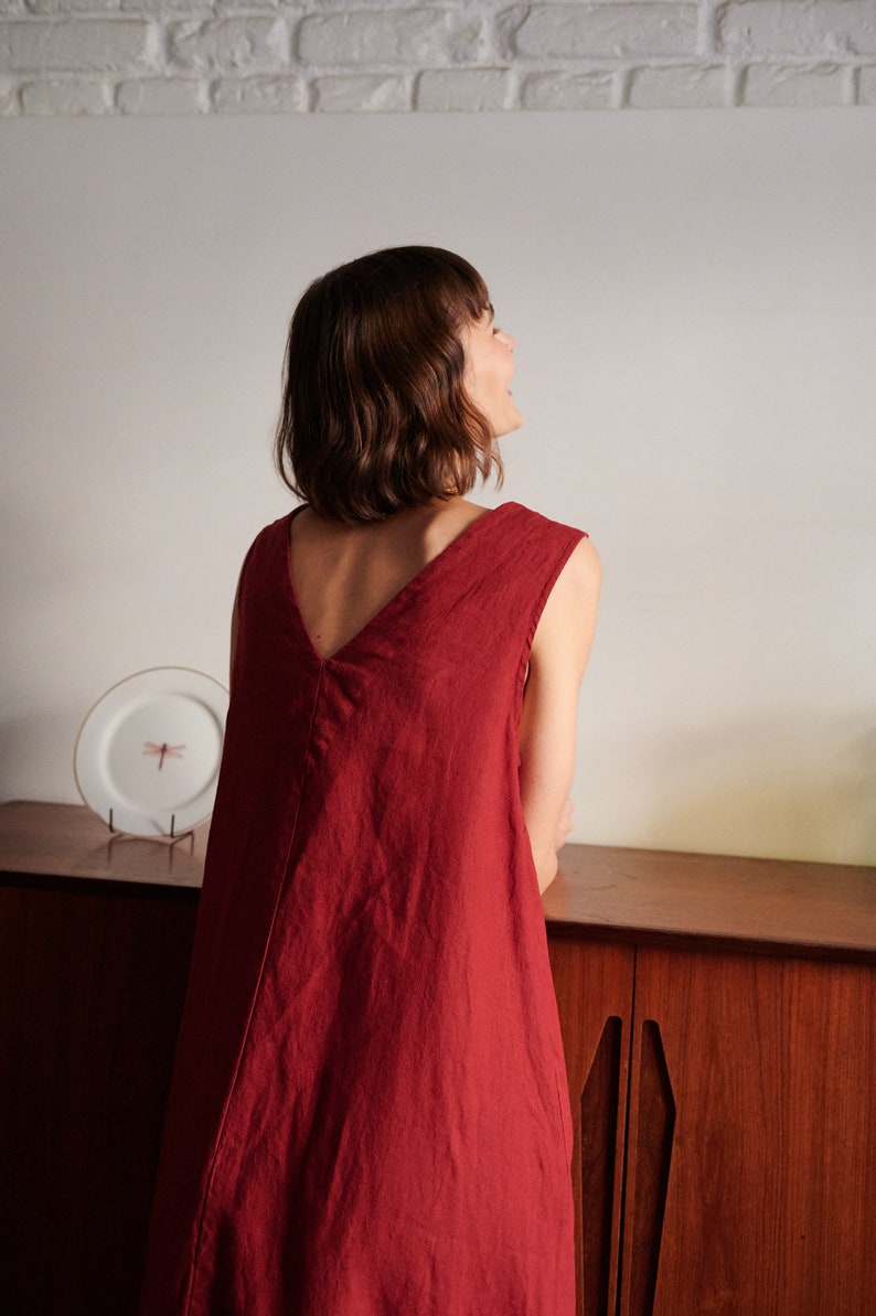 May include: A woman wearing a sleeveless, deep red linen dress with a V-neckline. The dress is loose-fitting and falls to her knees.