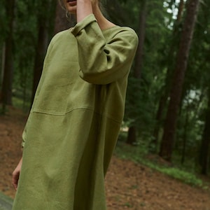 Peut inclure: Une femme portant une robe en lin ample de couleur vert olive &agrave; manches longues. Elle se tient dans un environnement forestier.