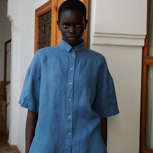 May include: A person wearing a blue linen shirt with a button-up front.
