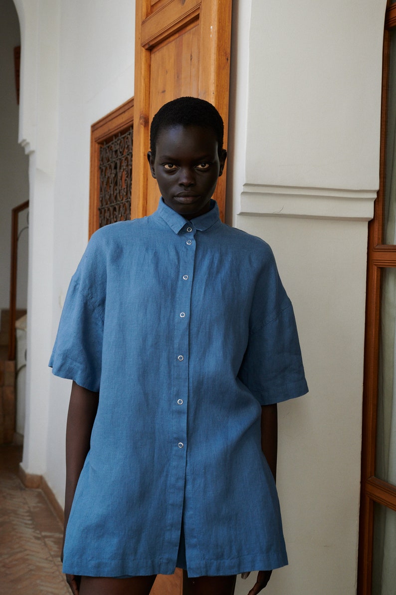 May include: A person wearing a blue linen shirt with a button-up front.