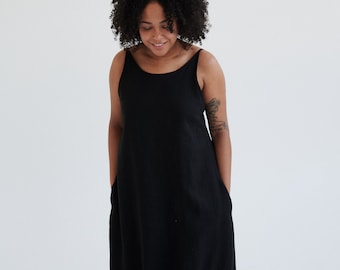 May include: A woman wearing a black sleeveless maxi dress with a scoop neck. The dress has pockets on the sides.